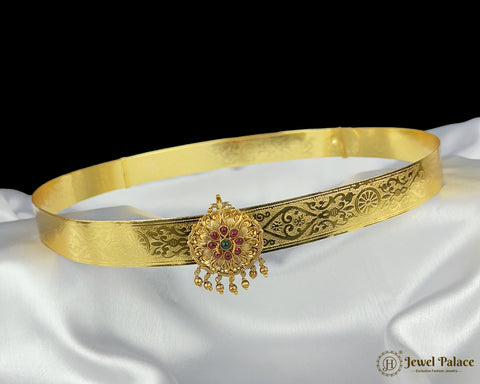 Gold belt with intricate designs and a central pendant on a white fabric background