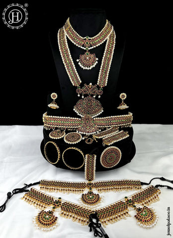 A traditional gold-plated Bharatanatyam jewelry set displayed on a mannequin, including a necklace, long chain, earrings, and various bangles with ornate designs.