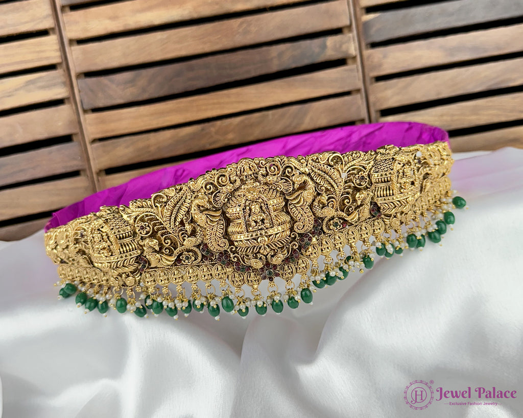 Decorative gold belt with green beads on a white fabric background