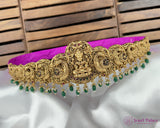 Gold necklace with green beads on a white surface with a wooden background