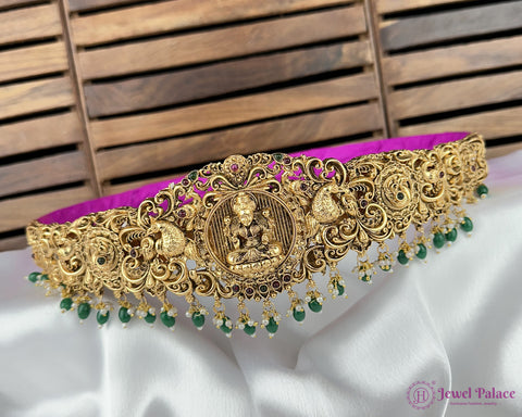 Gold necklace with green beads on a white and purple fabric background