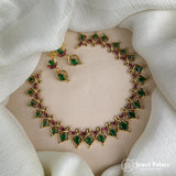 Gold necklace with green and red gemstones on a white fabric background, featuring the brand 'Jewel Palace'.