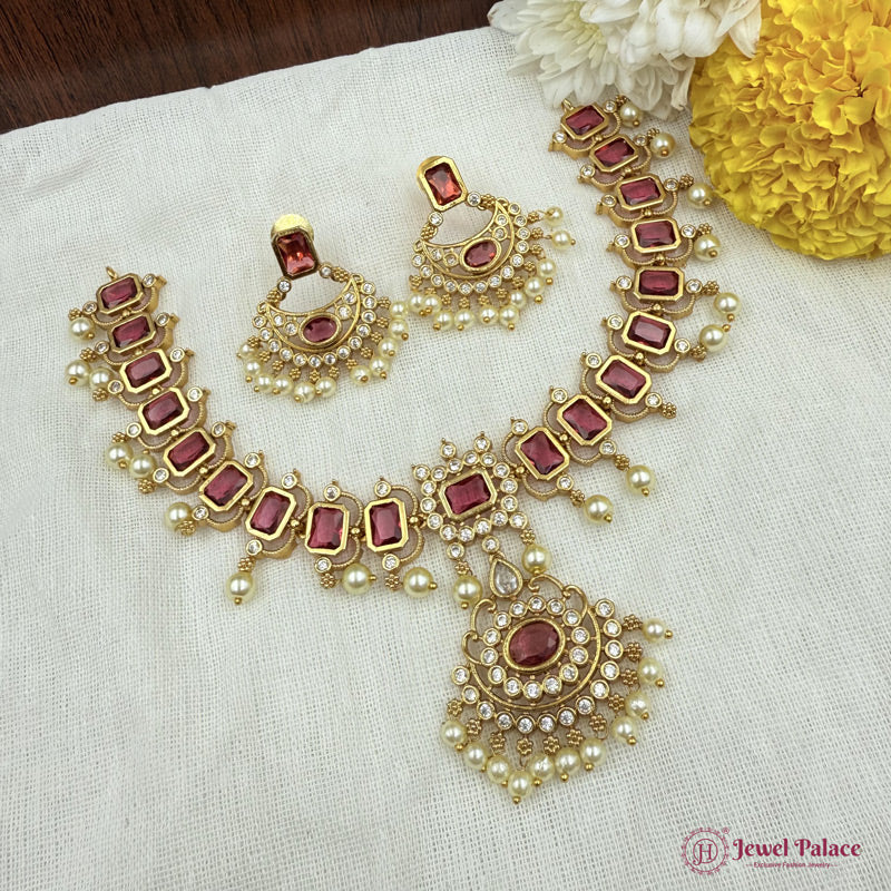 Ornate gold and red gemstone jewelry set on a white fabric background with flowers.