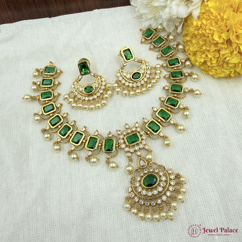 Gold necklace with green gemstones and pearl accents on a white fabric background.