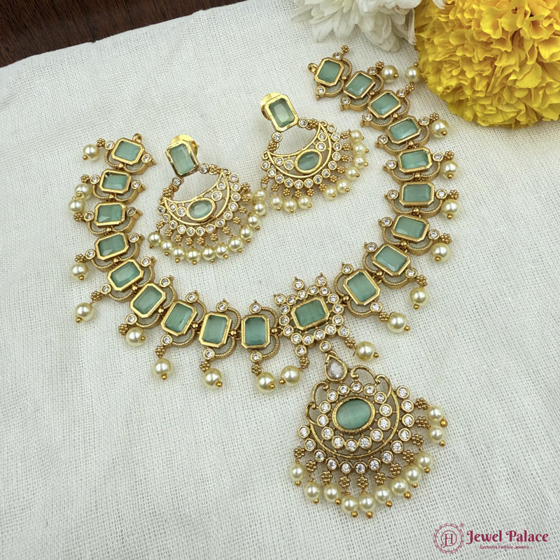 Ornate gold and green jewelry set on a white fabric background with yellow flowers.