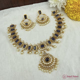 Ornate gold necklace with black stones and pearl-like beads on a white fabric background.