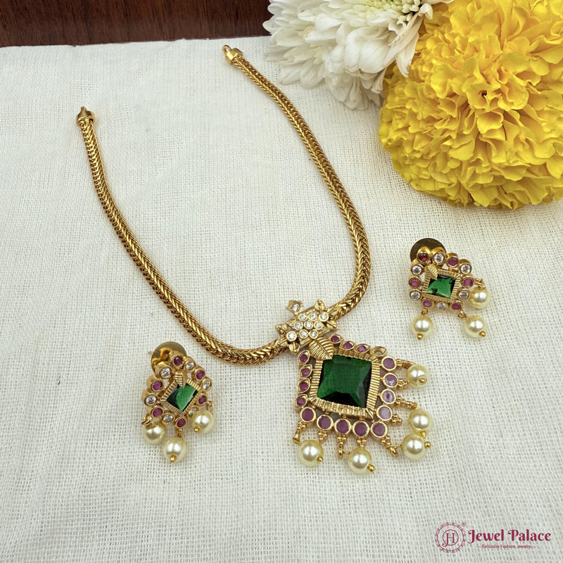Gold necklace with green and red gemstones on a white fabric background with yellow flowers.