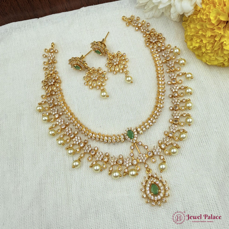 Gold necklace with green stones and matching earrings on a white fabric background with flowers.