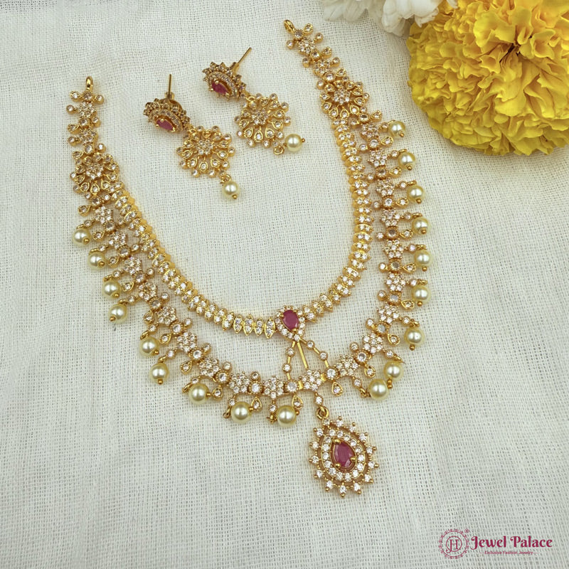 Gold necklace with pink stones and matching earrings on a white fabric background with yellow flowers.