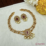 Gold necklace with red stones and pearl earrings on a white fabric background
