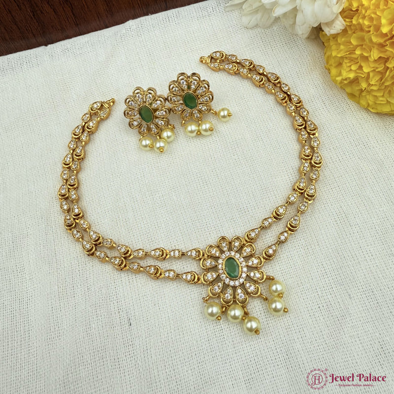 Gold necklace with green gemstones and matching earrings on a white fabric background.