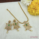 Gold necklace and earrings set with green stones on a white fabric background with yellow flowers.