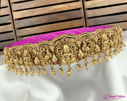 Gold necklace with intricate designs and red stones on a white and pink fabric background, brand 'Jewel Palace' visible.
