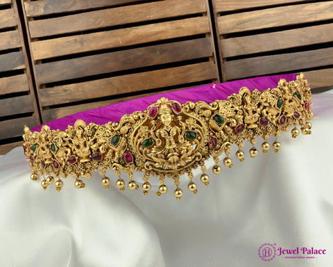 Gold jewelry with green and red stones on a white fabric background