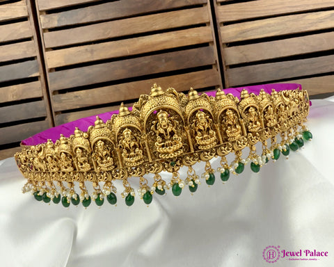 Decorative gold necklace with green beads on a white surface with wooden background