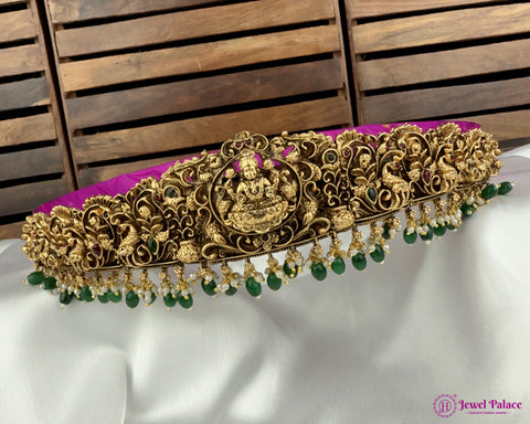 Decorative gold headband with green beads on a white and purple fabric background