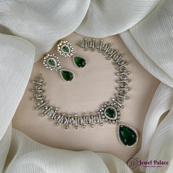 Jewelry set with necklace and earrings on a white fabric background, featuring green gemstones and silver accents.