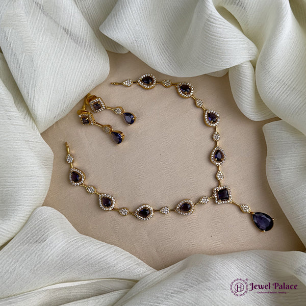 Gold necklace with purple stones on a beige surface surrounded by white fabric
