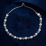 A silver-toned heart-link chain necklace with pavé-set clear stones, displayed on a textured dark navy blue fabric background.