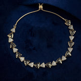 A gold necklace with triangular filigree and pavé-set clear stones, displayed on a dark navy blue velvet background.