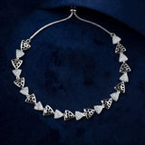 A silver-toned necklace with repeating openwork triangular links set with clear stones, displayed on a dark navy velvet surface.
