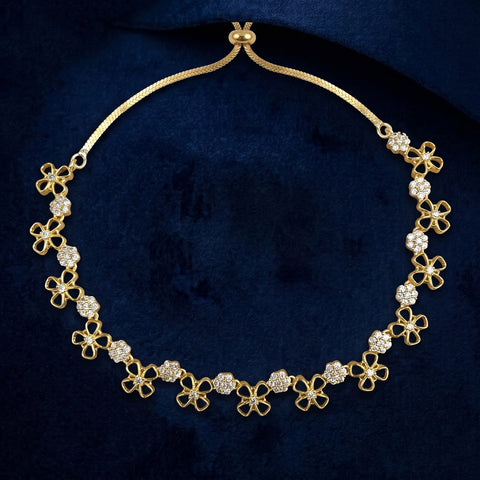 A gold-tone floral necklace with clear rhinestone accents, displayed on a textured dark blue velvet background.