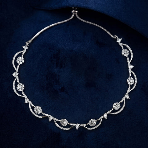 An ornate silver-toned necklace with floral and vine motifs set with clear stones, displayed on a dark navy velvet background.