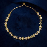 A gold chain necklace with repeating diamond-shaped links set with clear stones, displayed on a dark navy velvet surface.