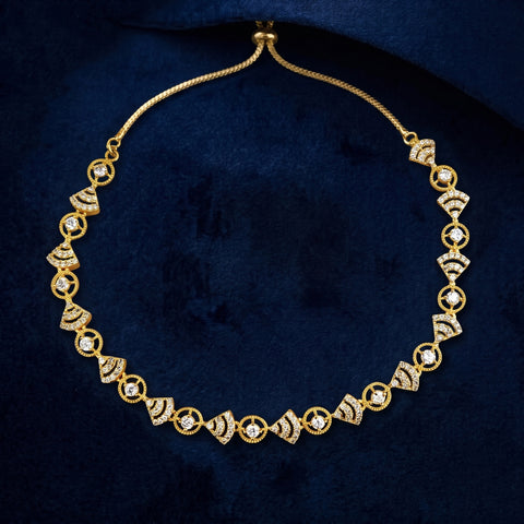 A gold chain necklace with repeating diamond-shaped links set with clear stones, displayed on a dark navy velvet surface.
