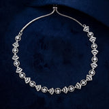 A silver-toned Art Deco style necklace with repeating fan and oval motifs set with clear stones, displayed on a dark navy velvet surface.