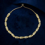 A gold chain necklace adorned with clusters of clear gemstones in floral and geometric motifs, displayed on a dark navy blue velvet background.