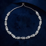 A silver-toned floral necklace with clear gemstones, displayed on a dark navy blue velvet background.