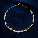 A gold chain necklace featuring repeating snowflake or starburst motifs paved with small clear stones, displayed on a dark navy velvet surface.