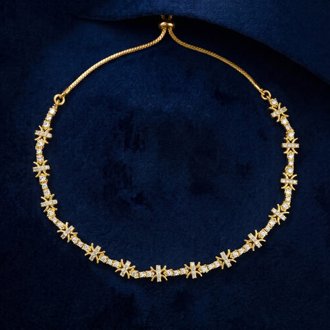 A gold chain necklace featuring repeating snowflake or starburst motifs paved with small clear stones, displayed on a dark navy velvet surface.