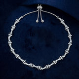 A silver-toned floral necklace with clear gemstones, displayed on a dark navy blue velvet background.