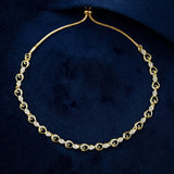 A gold chain necklace with alternating open heart links and rows of small clear stones, displayed on a dark navy velvet surface.