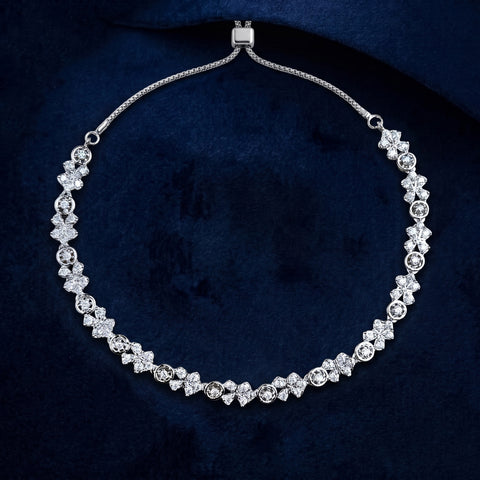 A silver-toned floral necklace with clear gemstones, displayed on a dark navy blue velvet background.