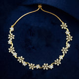 A gold chain necklace featuring multiple snowflake-shaped clusters of clear stones, displayed on a dark navy velvet background.