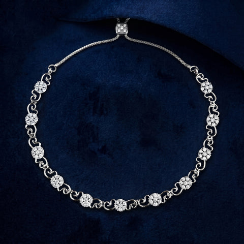 A silver-toned diamond tennis necklace with floral and scroll motifs, displayed on a dark navy blue velvet background.
