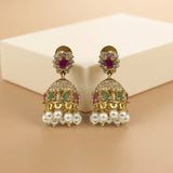 A pair of gold-plated Indian Jhumka earrings with white faux pearls, purple and green stones, and clear crystals, displayed on a beige background with a cream-colored box.