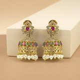 A pair of gold-plated Indian jhumka earrings with pink and green stone accents, clear crystal details, and dangling white faux pearls, displayed on a beige background with a white block.