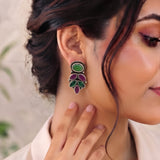 A close-up lifestyle shot of a woman wearing a silver-toned leaf-shaped earring with green and purple stones, touching her neck to show the scale.
