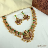 Gold necklace with green and red stones on a white surface, branded 'Jewel Palace'.