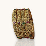 Set of gold bangles with gemstones on a white background
