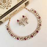 Gold-toned traditional necklace and matching earrings set with clear stones and red gemstone accents, arranged on a light cream background beside an ornate decorative book.