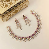 A silver-toned Indian ethnic jewelry set featuring a necklace and matching earrings decorated with clear teardrop-shaped crystals and magenta-pink floral accents, displayed on a cream-colored surface next to a decorative gold and black box.