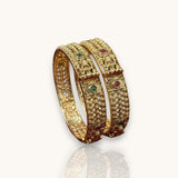 Pair of gold bangles with gemstones on a white background