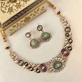 An ornate Indian ethnic jewelry set featuring a statement necklace and matching earrings. The set is embellished with silver-toned metal, light green stone inlays, clear rhinestones, black enamel, and pink enamel accents.