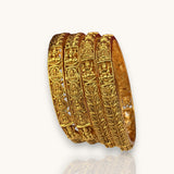 Set of gold bangles with intricate designs on a white background