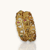 Gold bracelet with intricate designs and gemstones on a white background